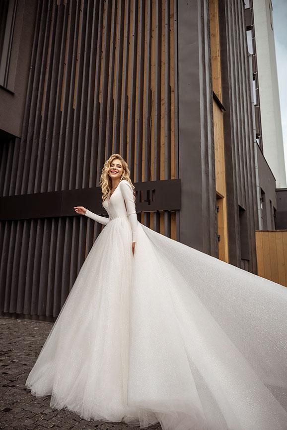 A woman in a long white wedding dress is standing in front of a building.