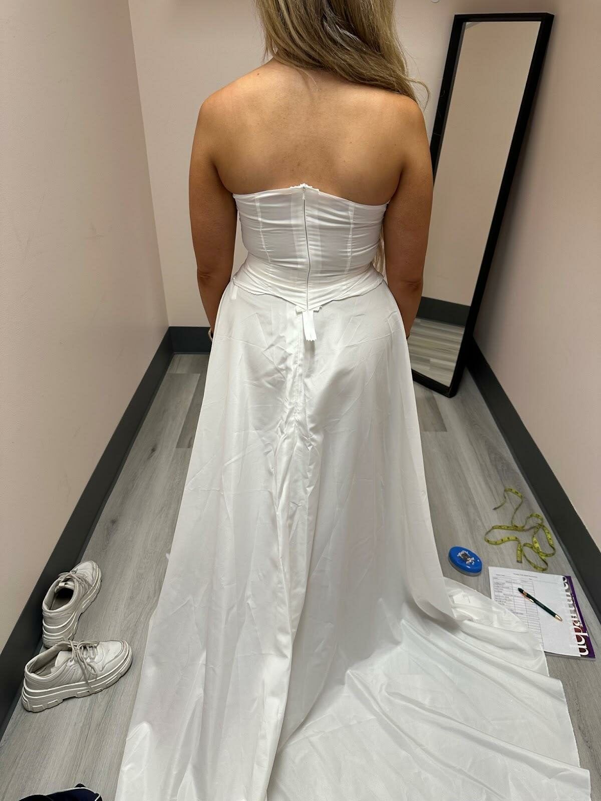 A woman is wearing a white wedding dress in a dressing room.