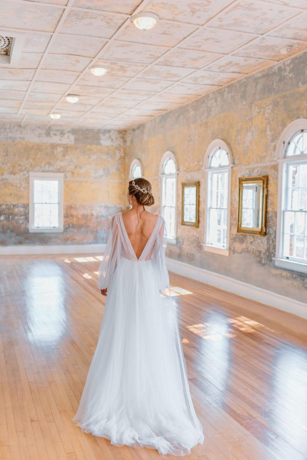 A bride in a white wedding dress is standing in a room with a wooden floor.