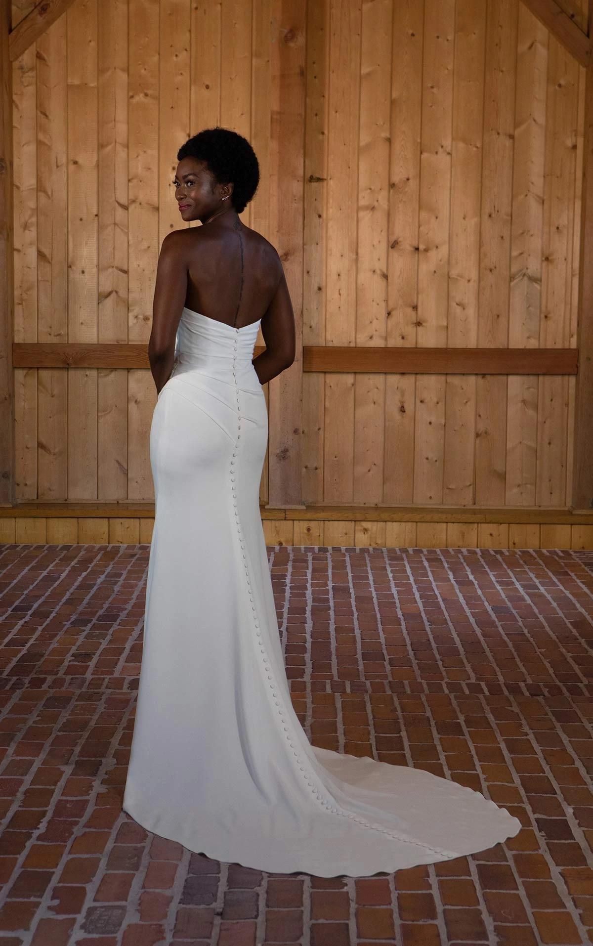 A woman in a white wedding dress is standing in front of a wooden wall.