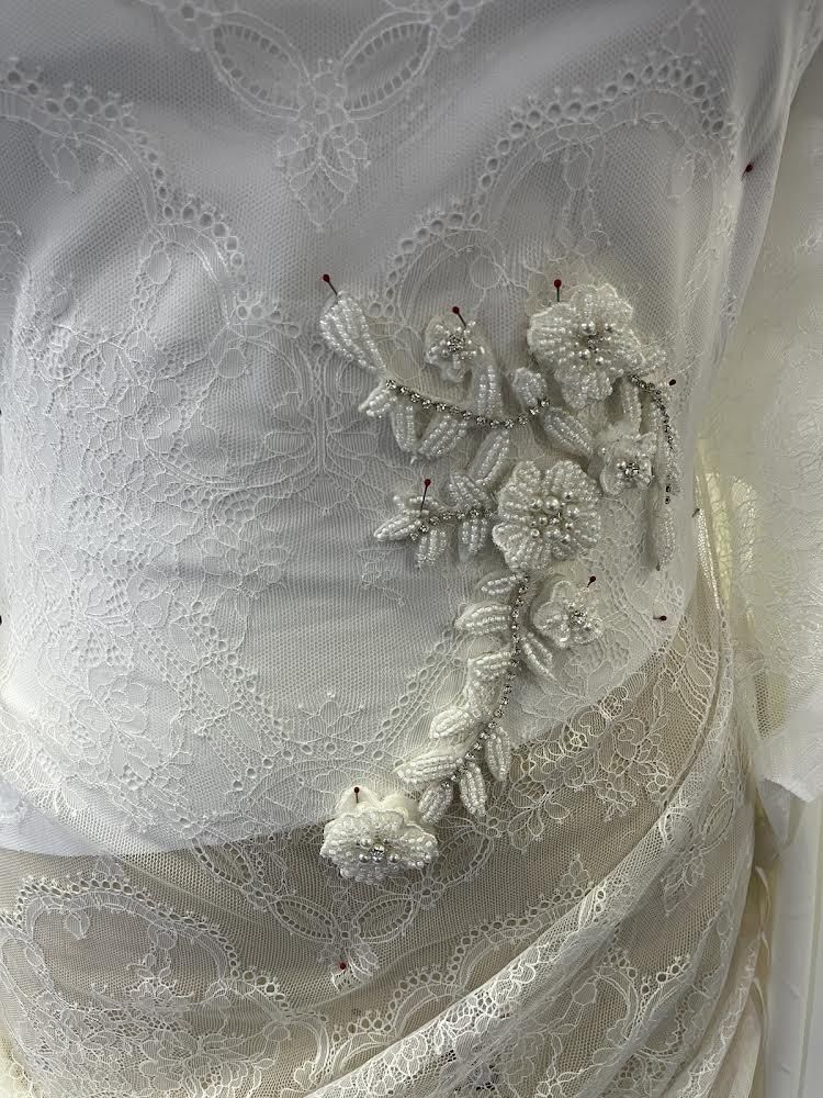A close up of a white lace dress with flowers on it.