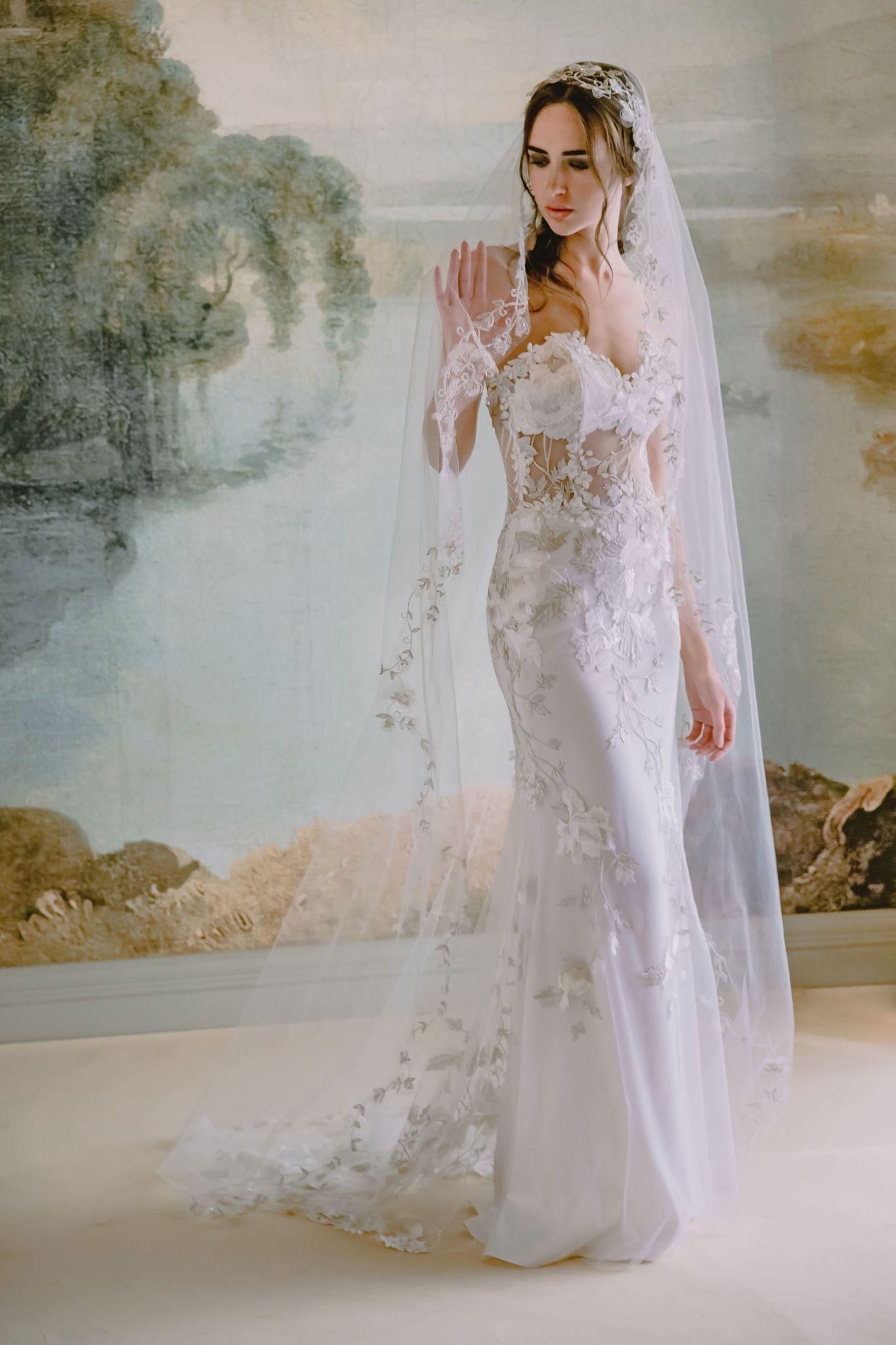 A woman in a wedding dress and veil is standing in front of a painting.