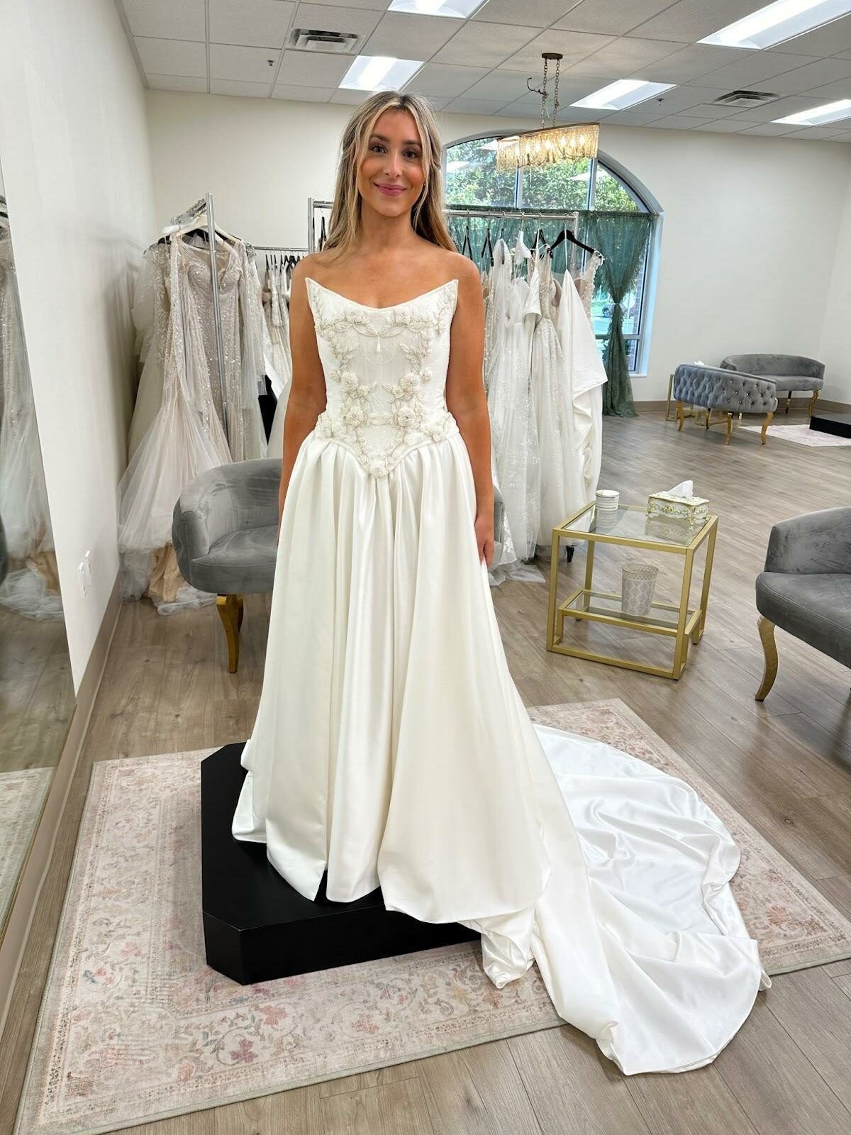 A woman in a white wedding dress is standing in a bridal shop.