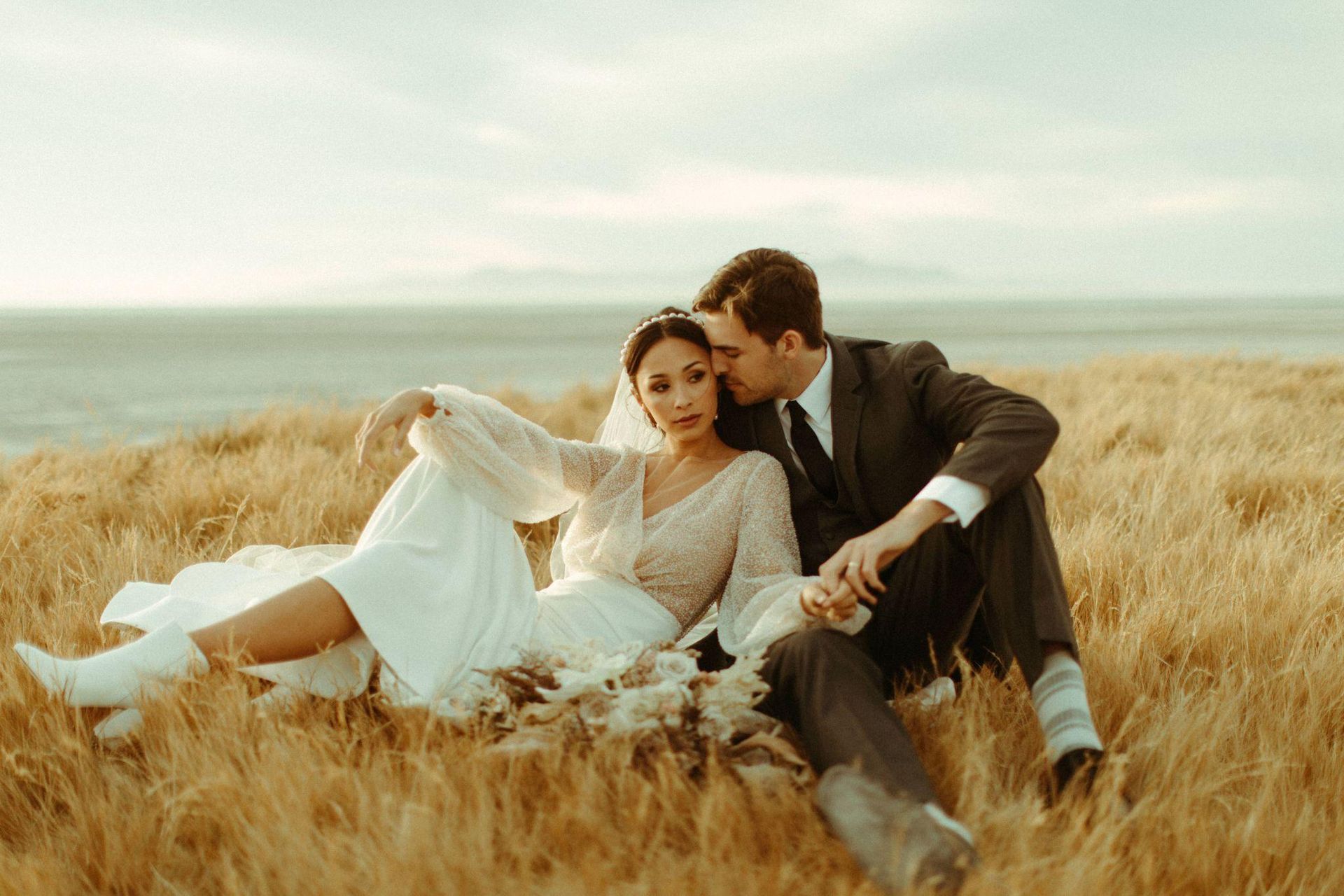 A bride and groom are sitting in a field of wheat.