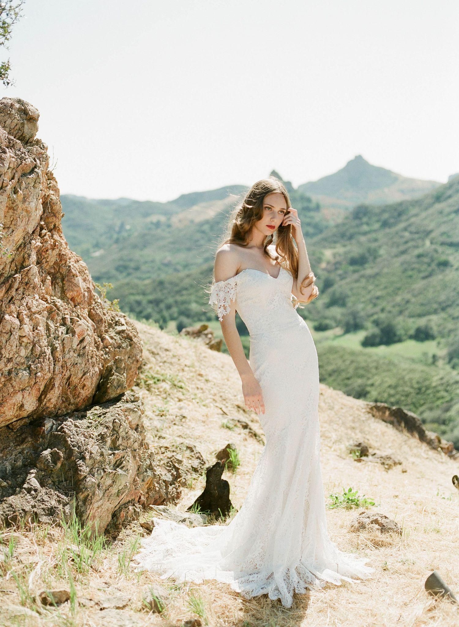 A woman in a wedding dress is standing on top of a hill.