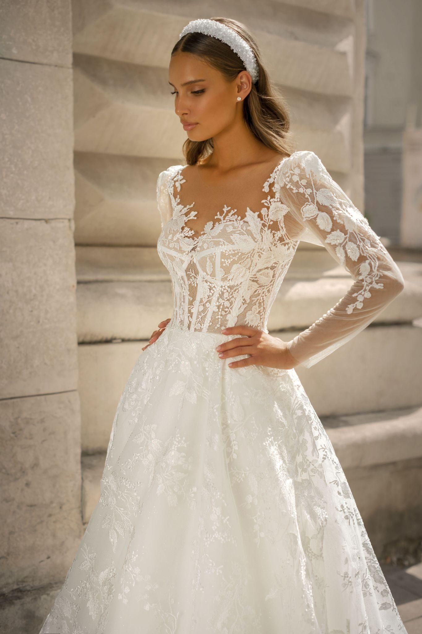 A woman is wearing a white wedding dress with long sleeves and a headband.