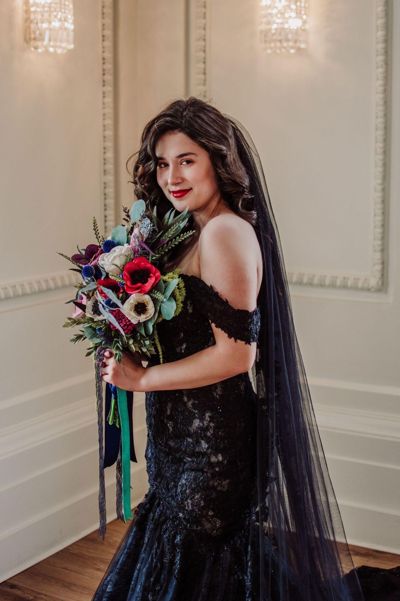 A woman in a black dress and veil is holding a bouquet of flowers.