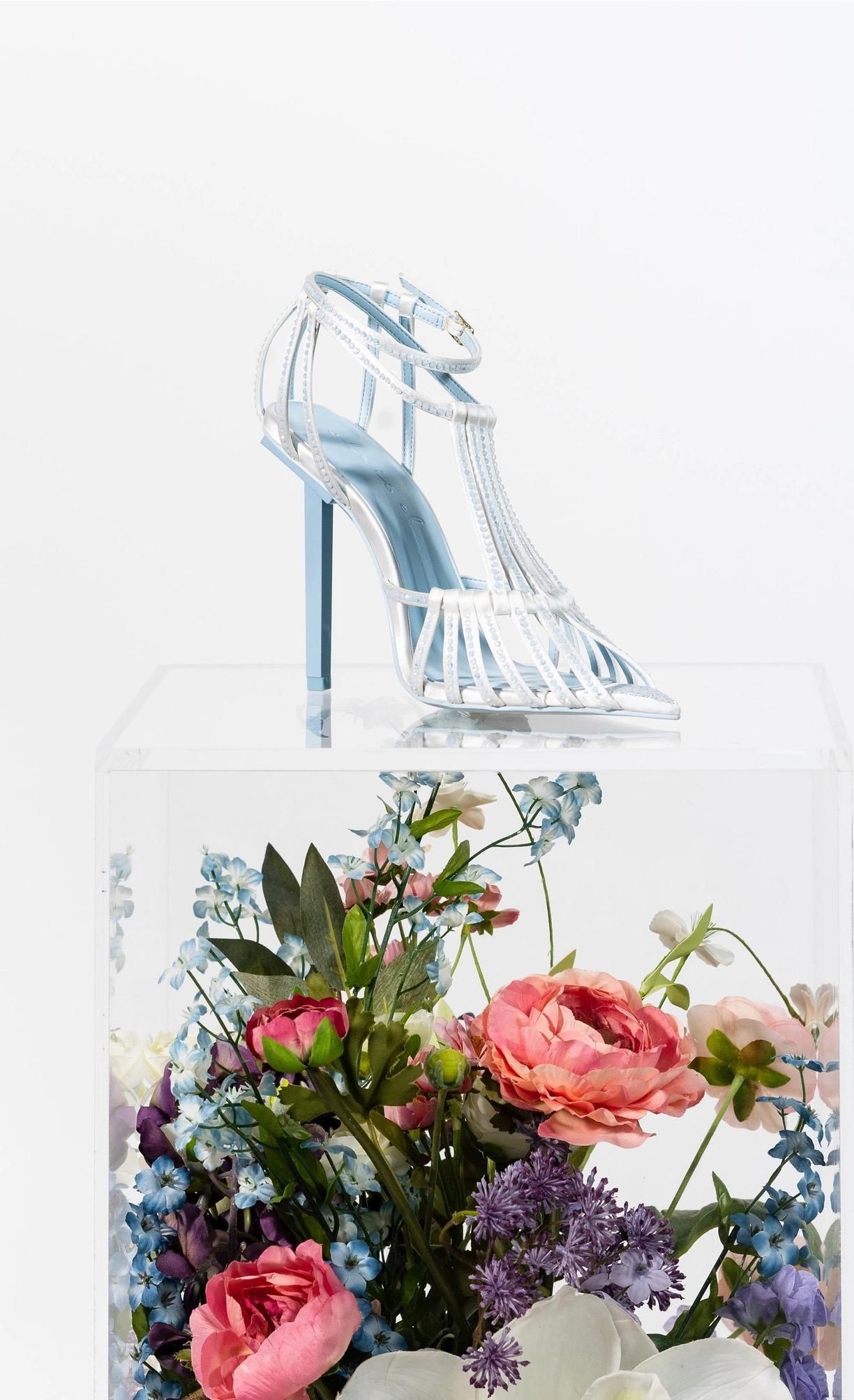 A shoe is sitting on top of a clear box surrounded by flowers.