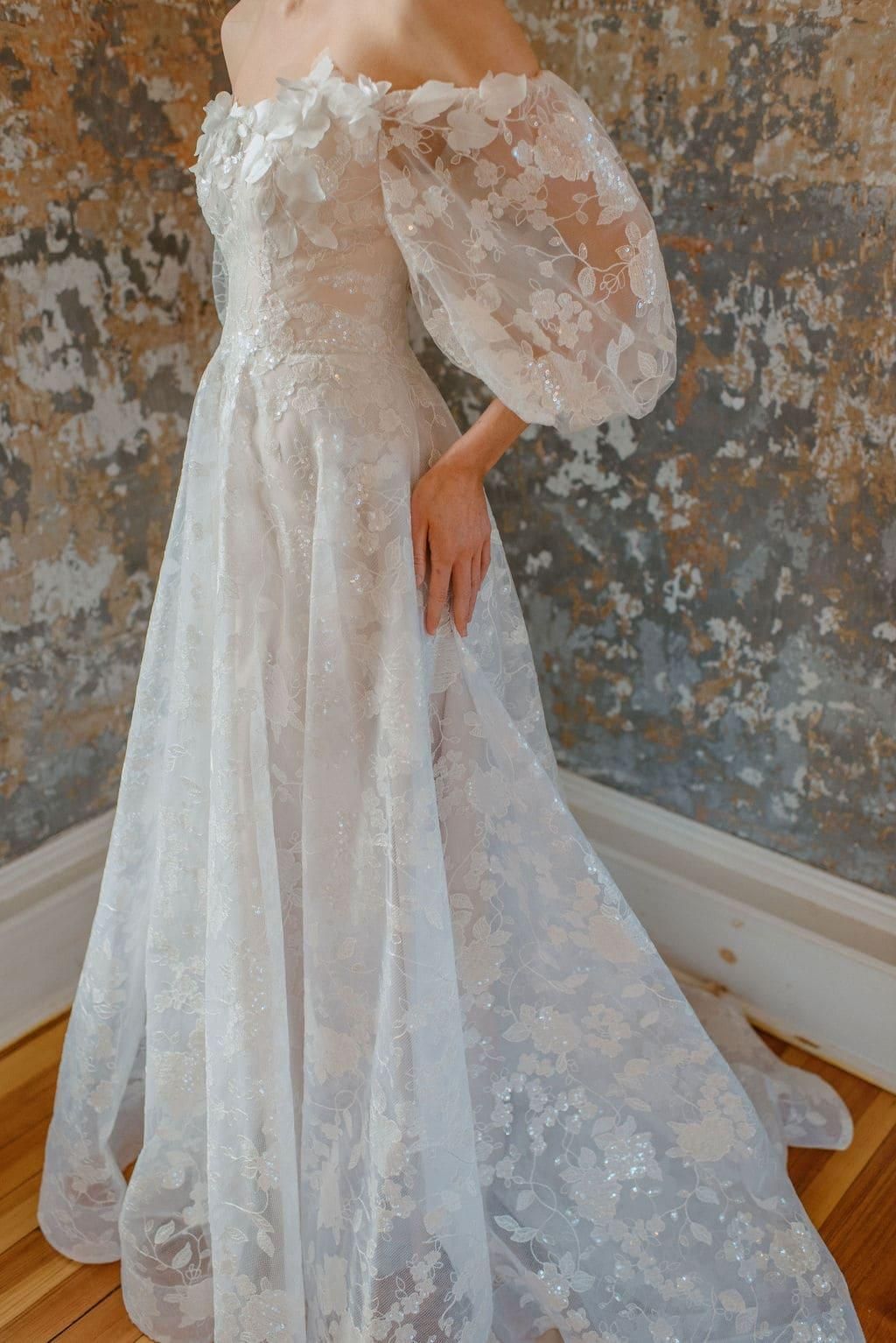 A woman is wearing a white lace wedding dress with puffed sleeves.