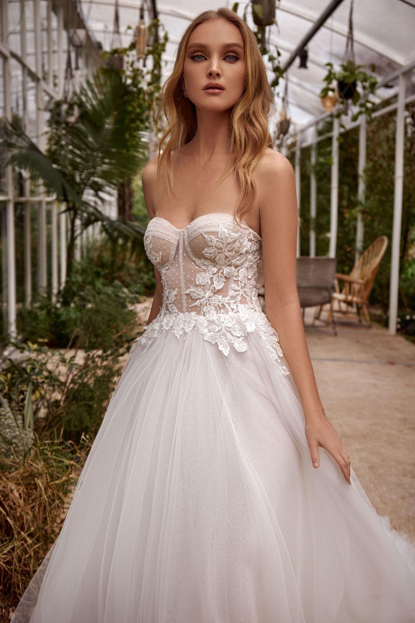 A woman in a white wedding dress is standing in a greenhouse.