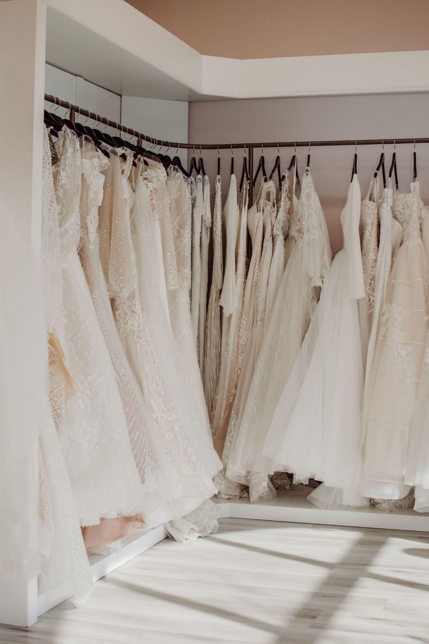 A room filled with lots of white dresses hanging on racks.