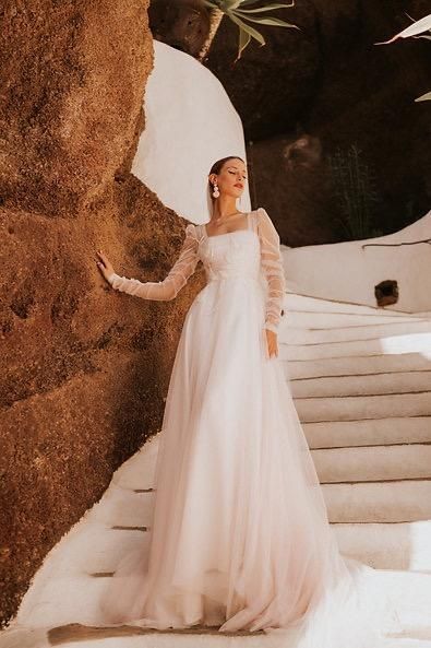 A woman in a wedding dress is standing next to a rock.