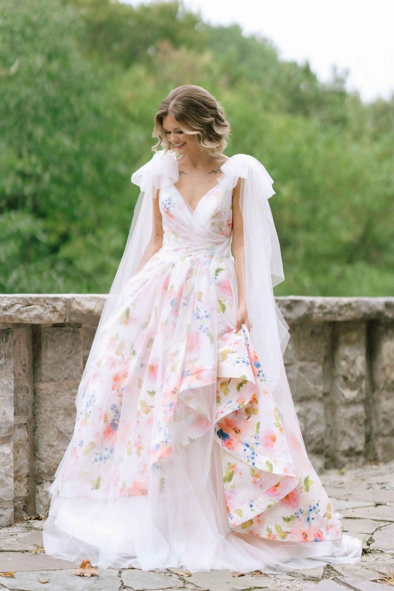 A bride in a floral wedding dress is standing on a stone bridge.