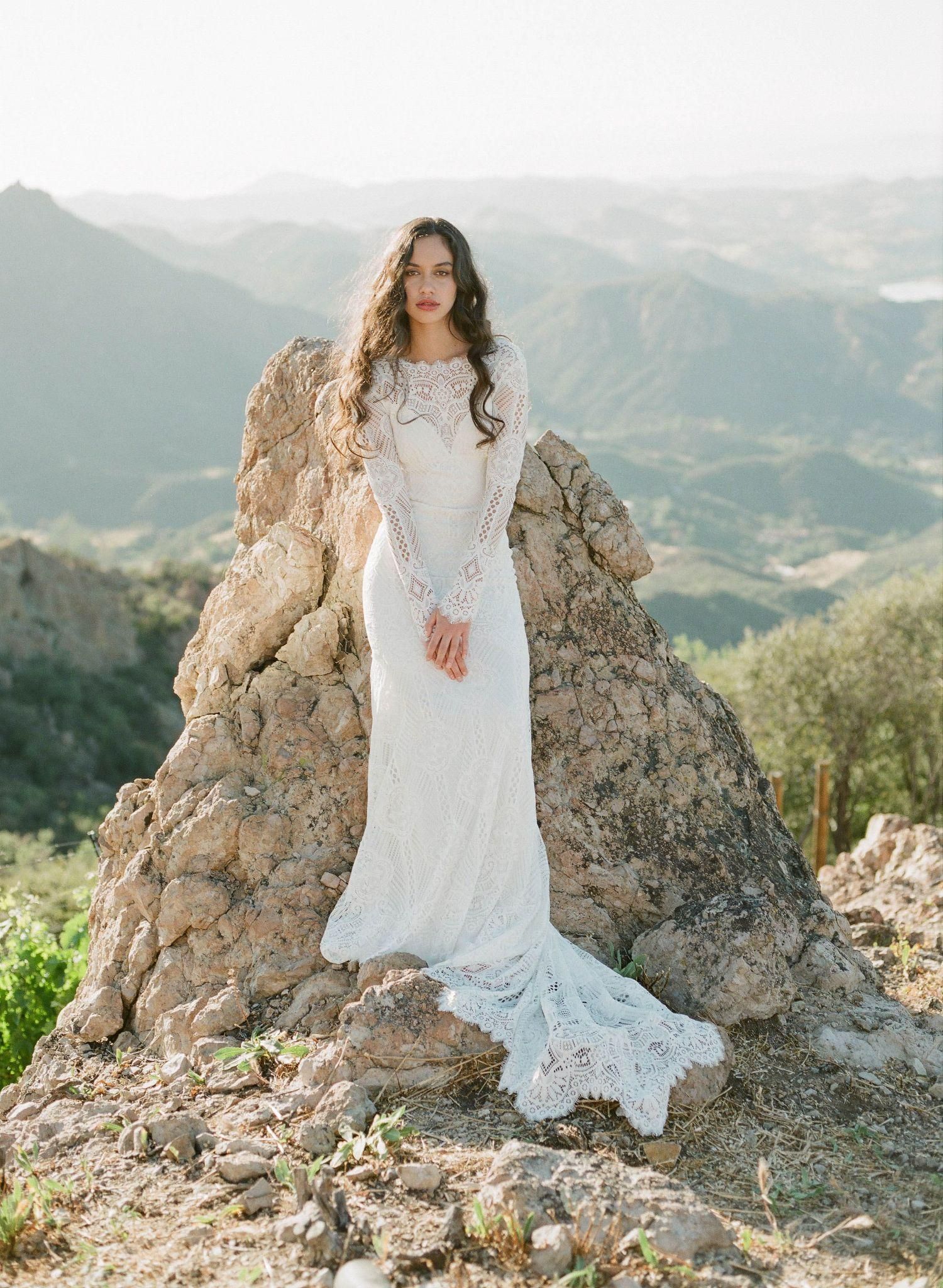 A woman in a white dress is standing on top of a rock.