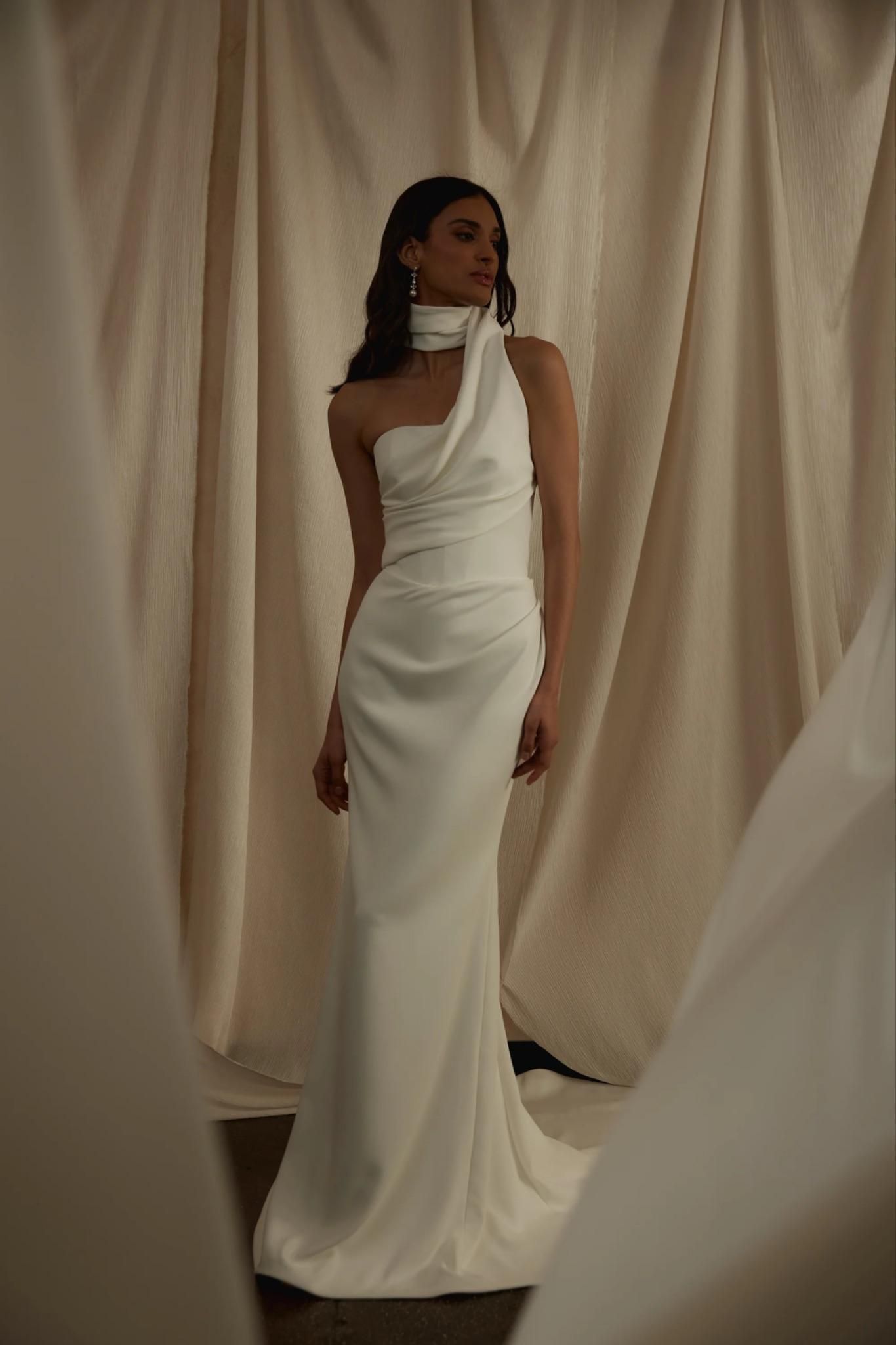 A woman in a white dress is standing in front of a white curtain.