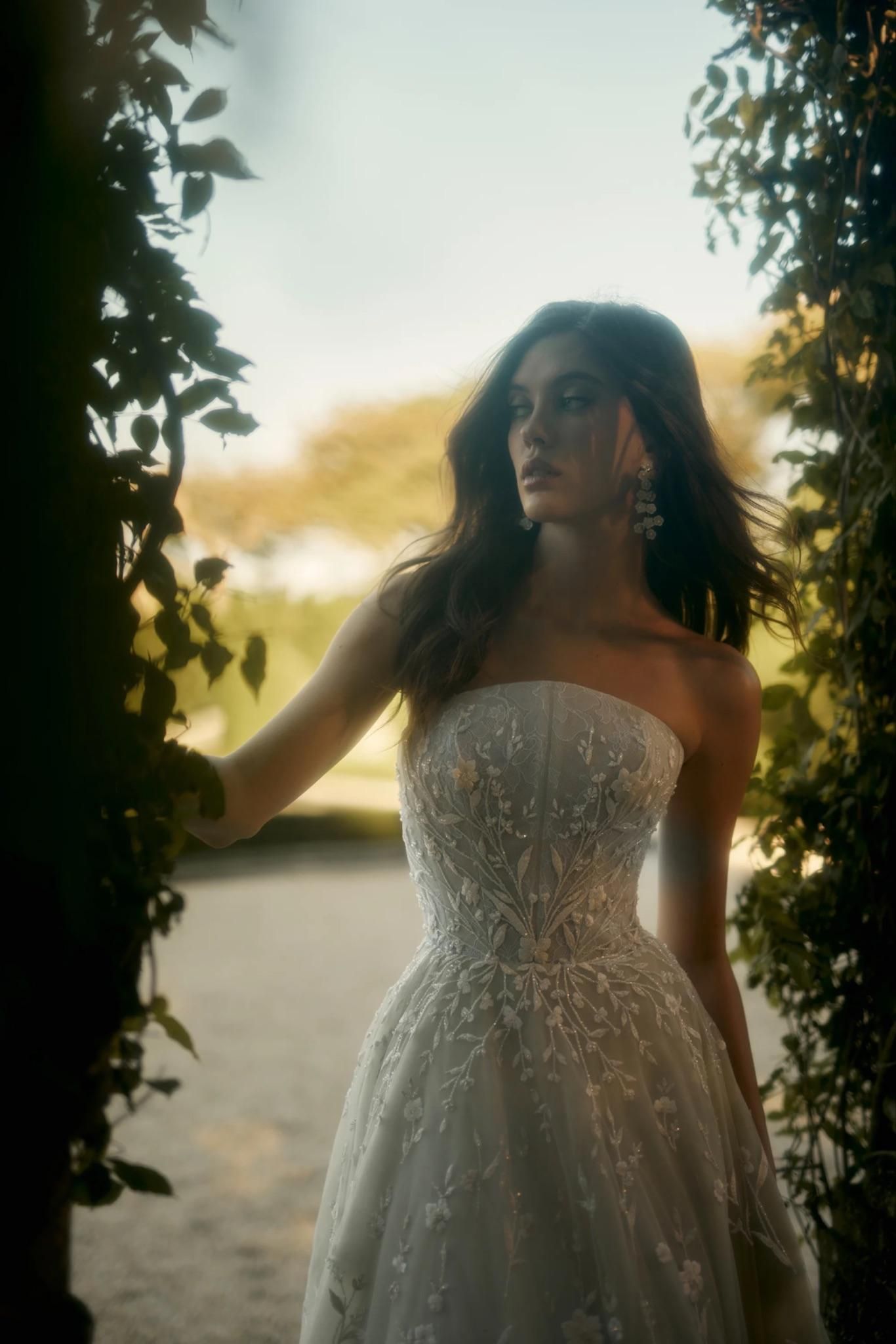 A woman in a wedding dress is standing next to a tree.