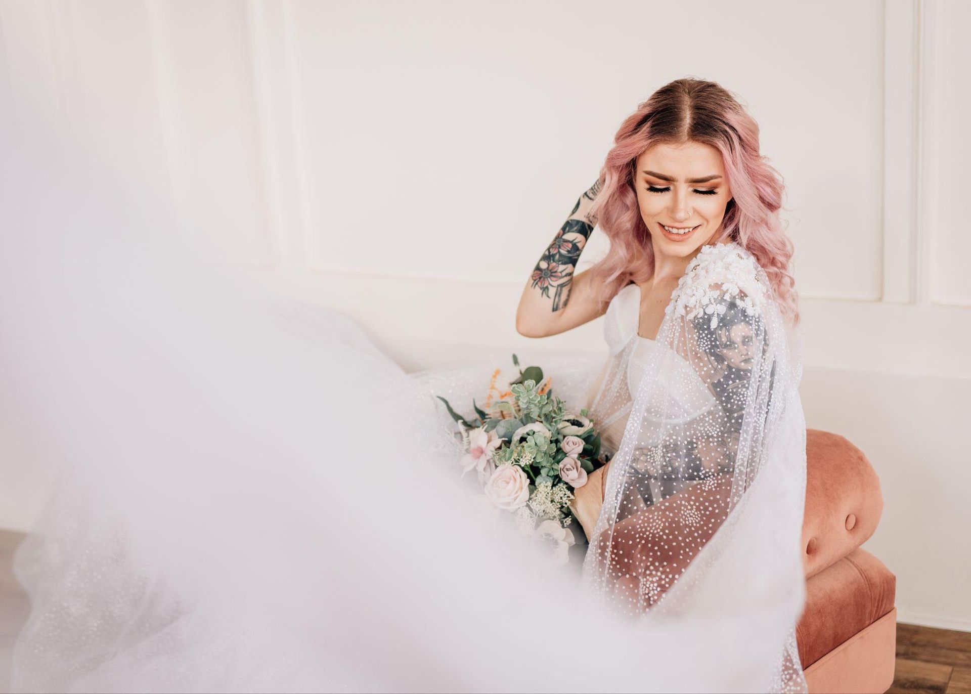 A woman in a wedding dress is sitting on a couch holding a bouquet of flowers.