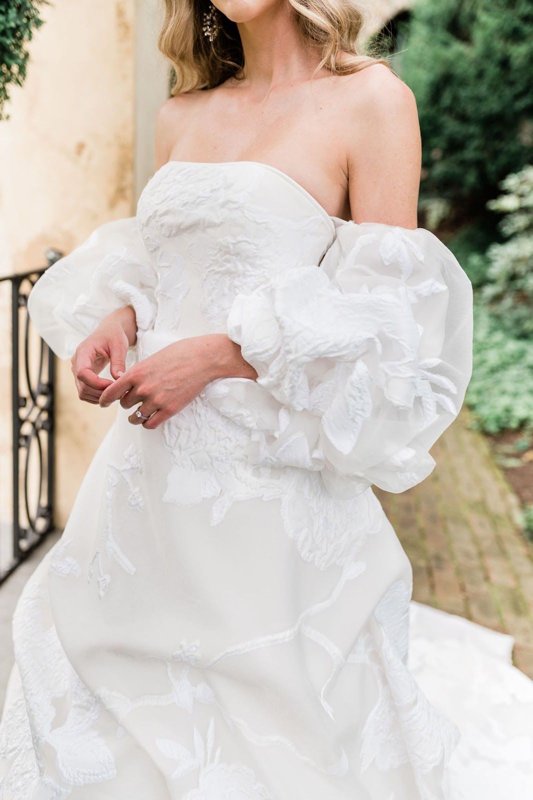 A woman in a white wedding dress with puffed sleeves is standing next to a railing.