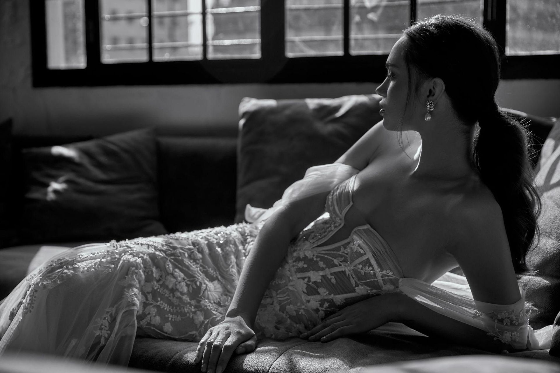 A woman in a wedding dress is laying on a couch in front of a window.