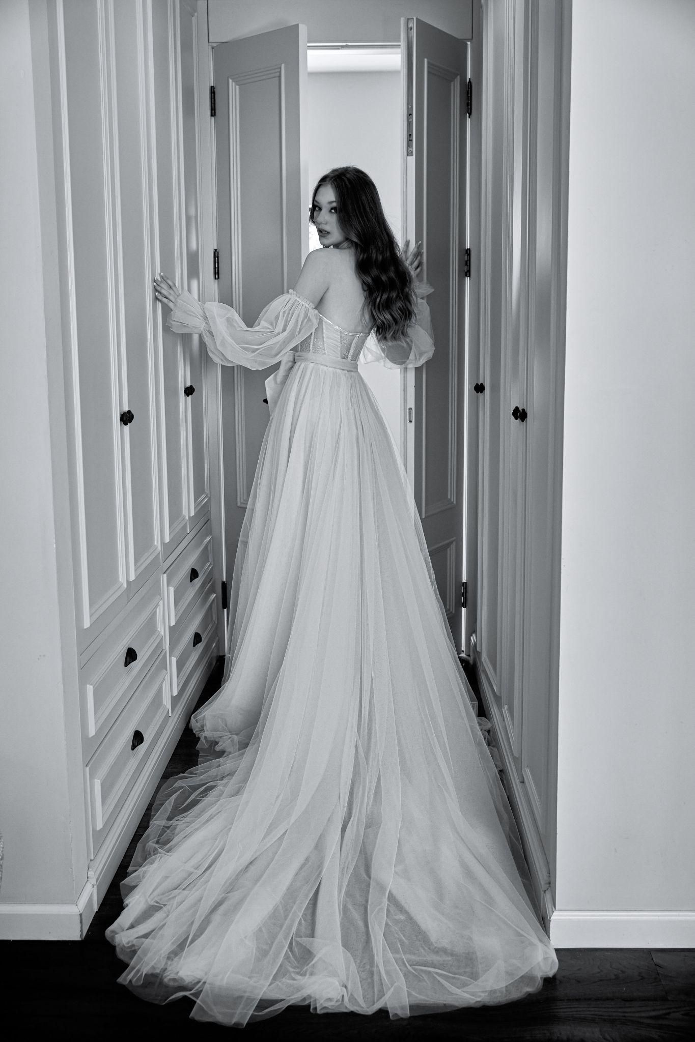 A black and white photo of a woman in a wedding dress standing in a hallway.