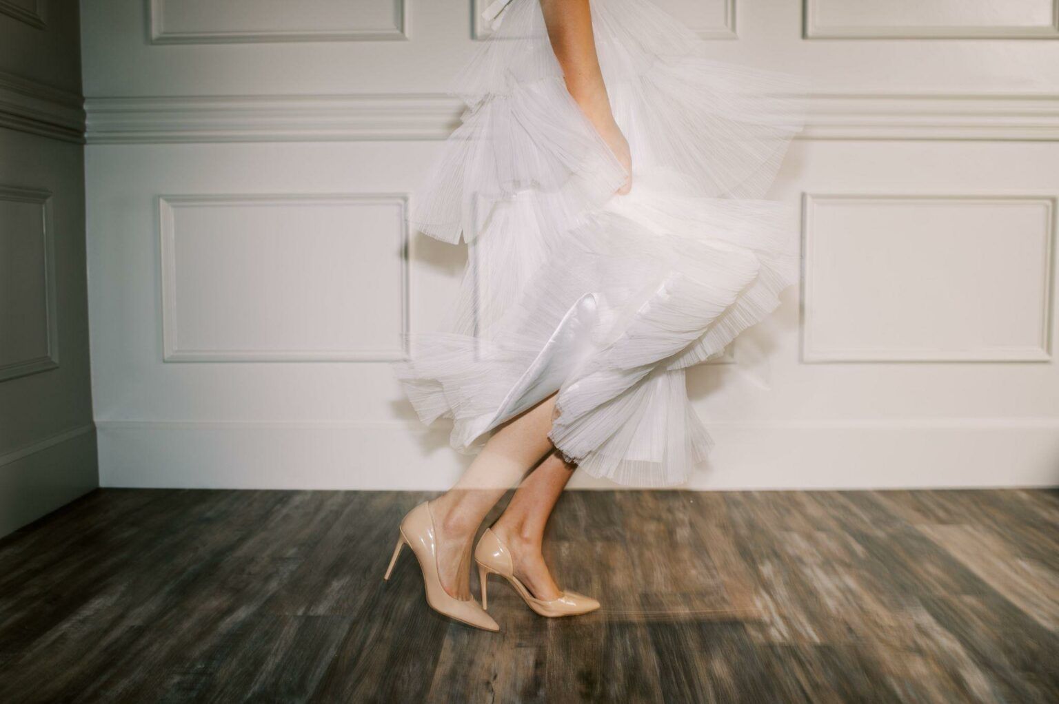 A woman in a white dress and high heels is dancing on a wooden floor.