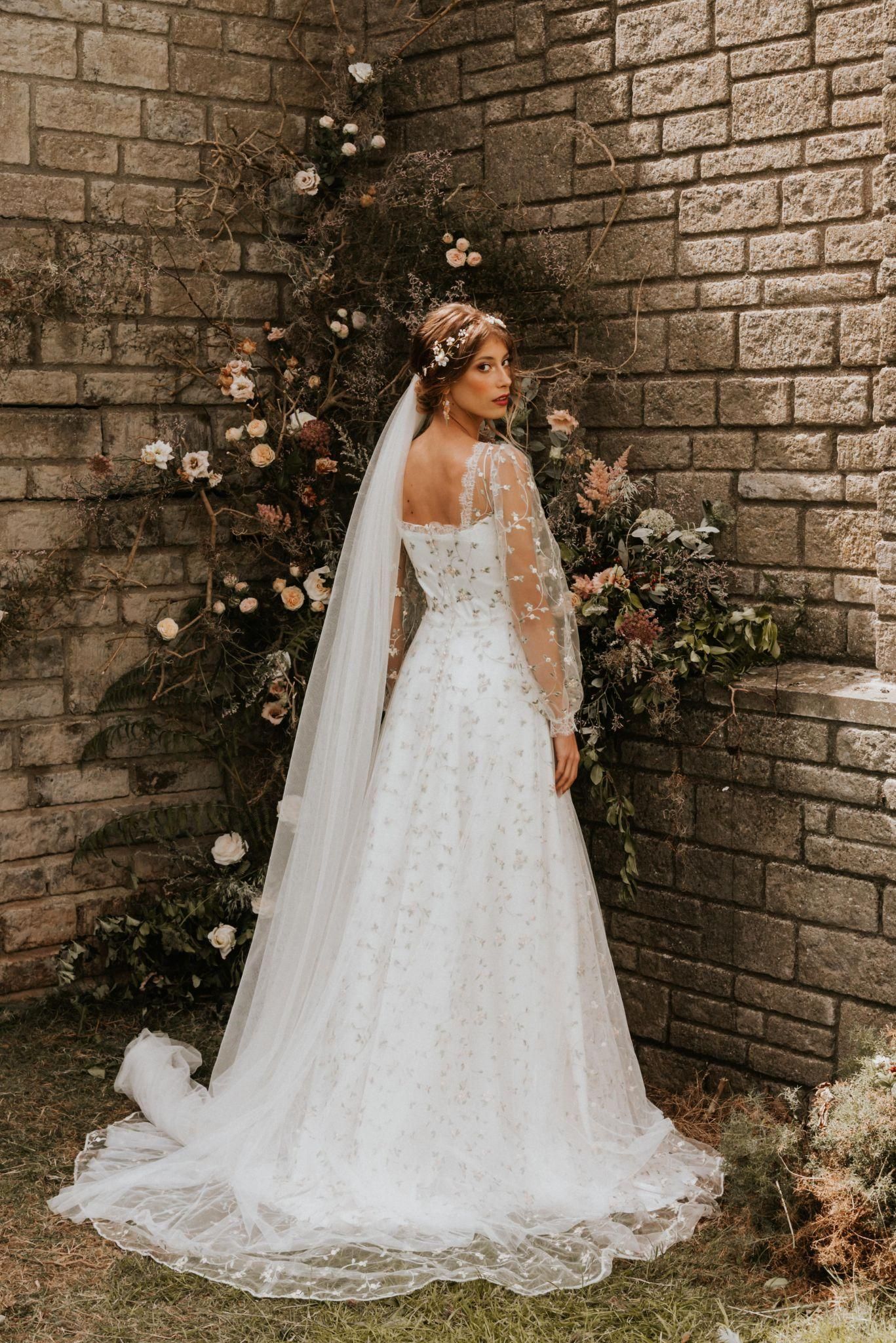 A woman in a wedding dress and veil is standing in front of a brick wall.
