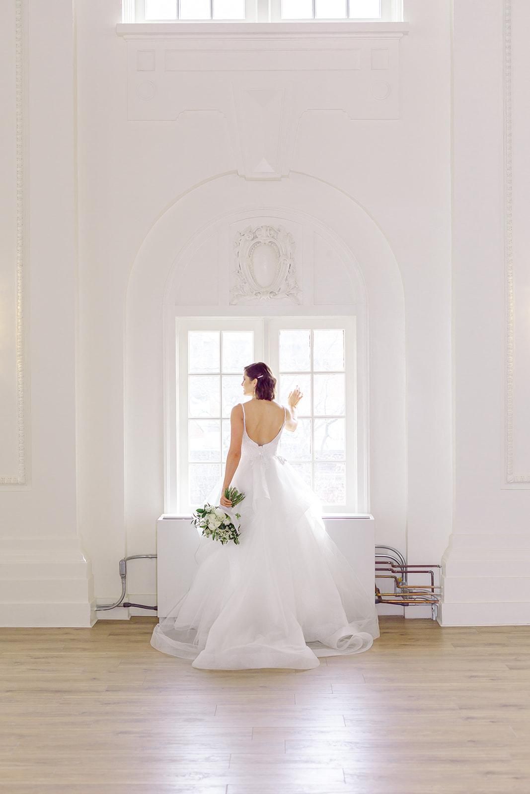A bride in a wedding dress is standing in front of a window holding a bouquet of flowers.