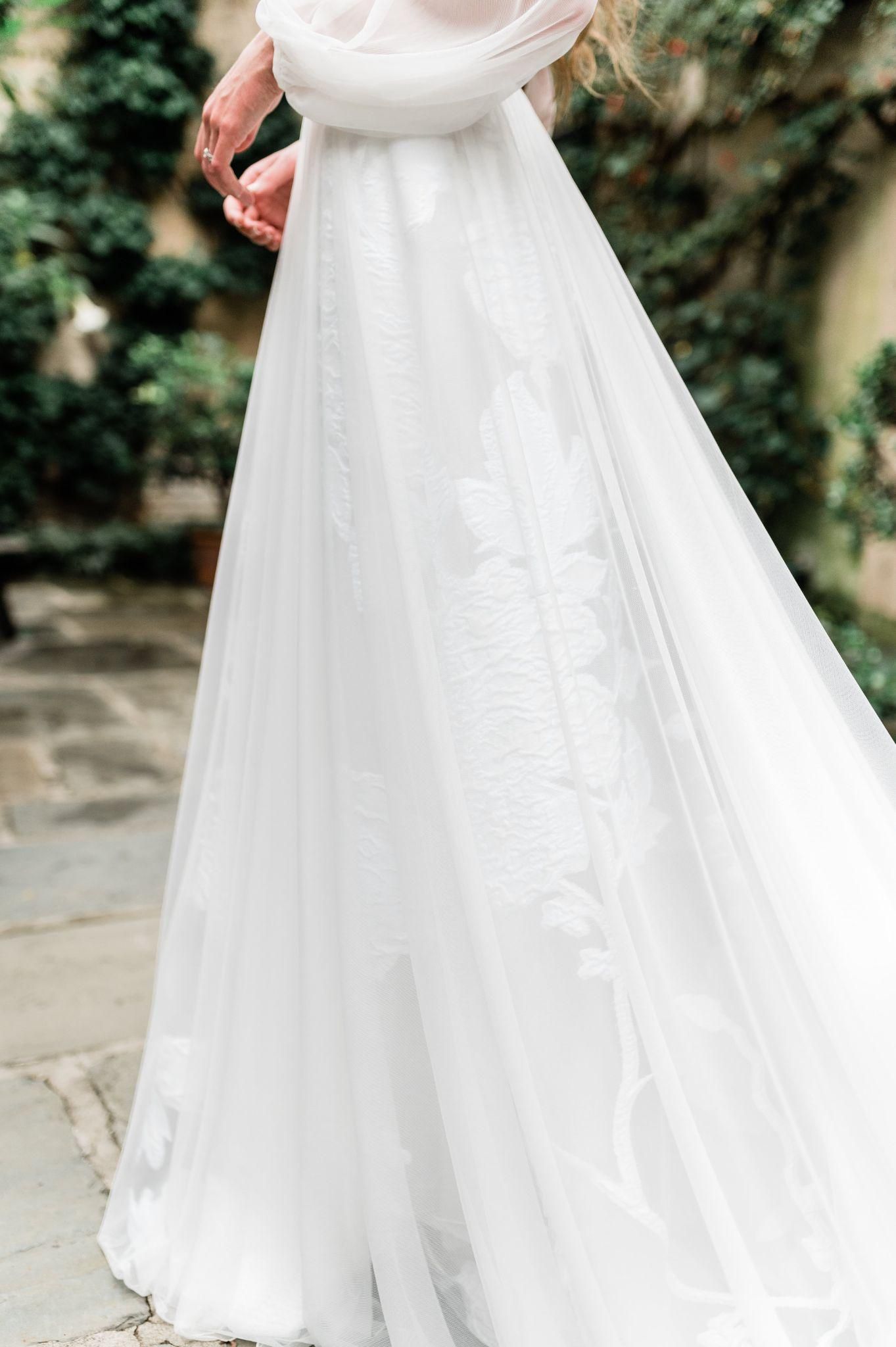 A woman in a white wedding dress is standing on a sidewalk.