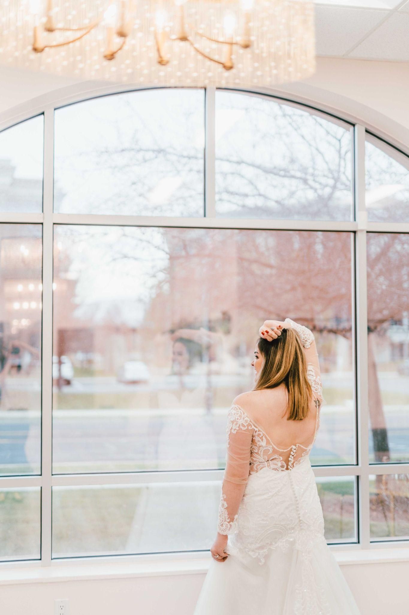 A bride in a wedding dress is standing in front of a large window.