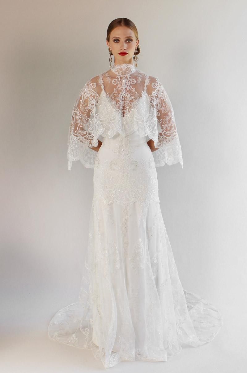 A woman is wearing a white lace wedding dress with a cape.