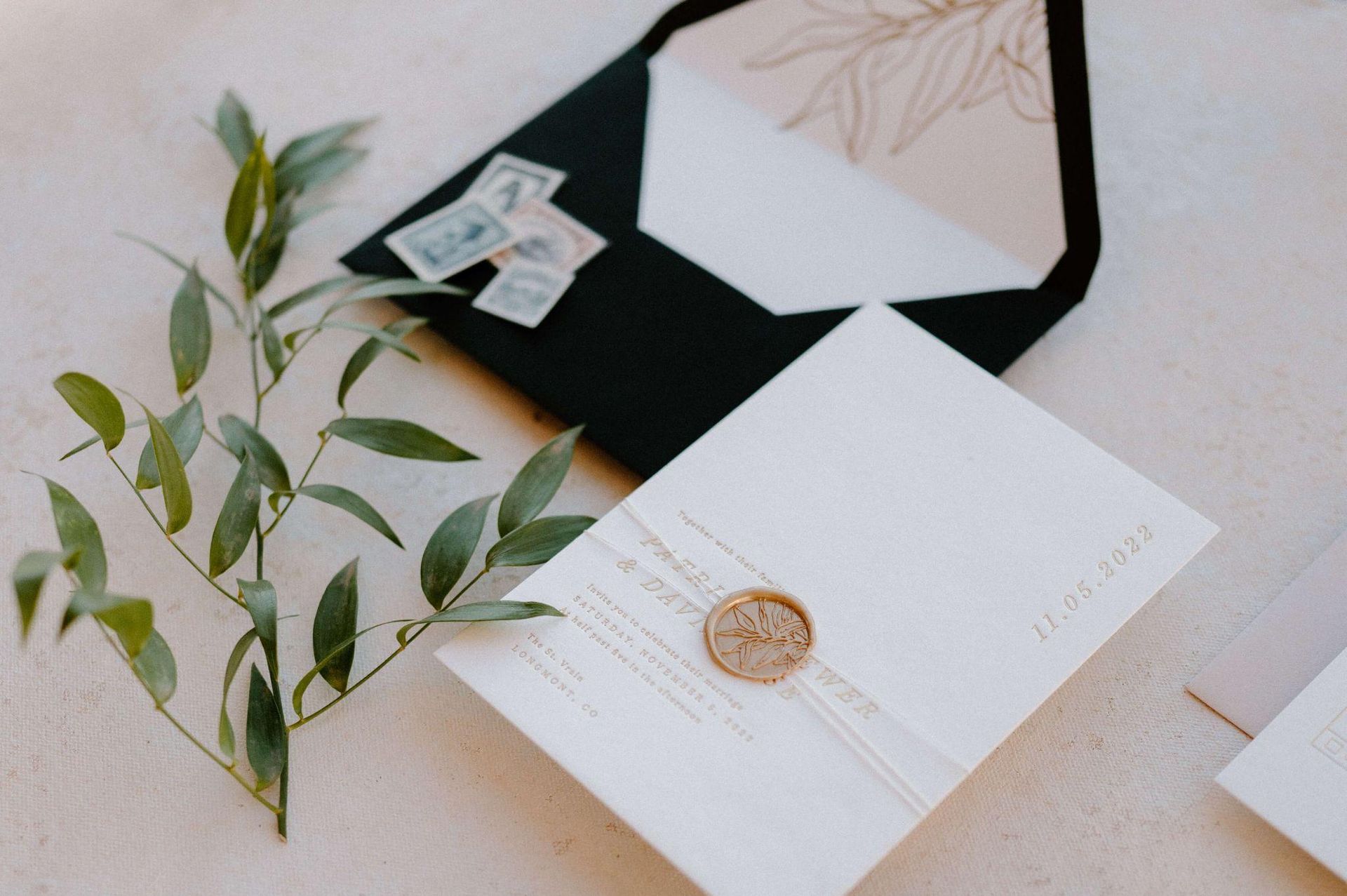 A wedding invitation is sitting on a table next to a black envelope.