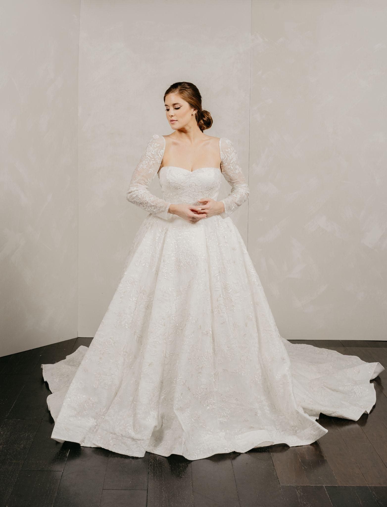 A woman is wearing a white wedding dress with long sleeves and a train.