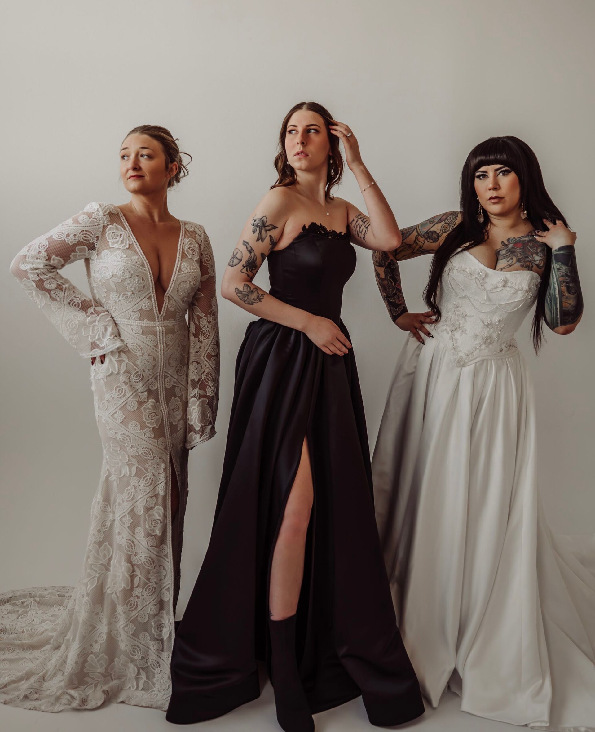 Three women in wedding dresses are standing next to each other with the woman in the middle in a Black wedding dress.