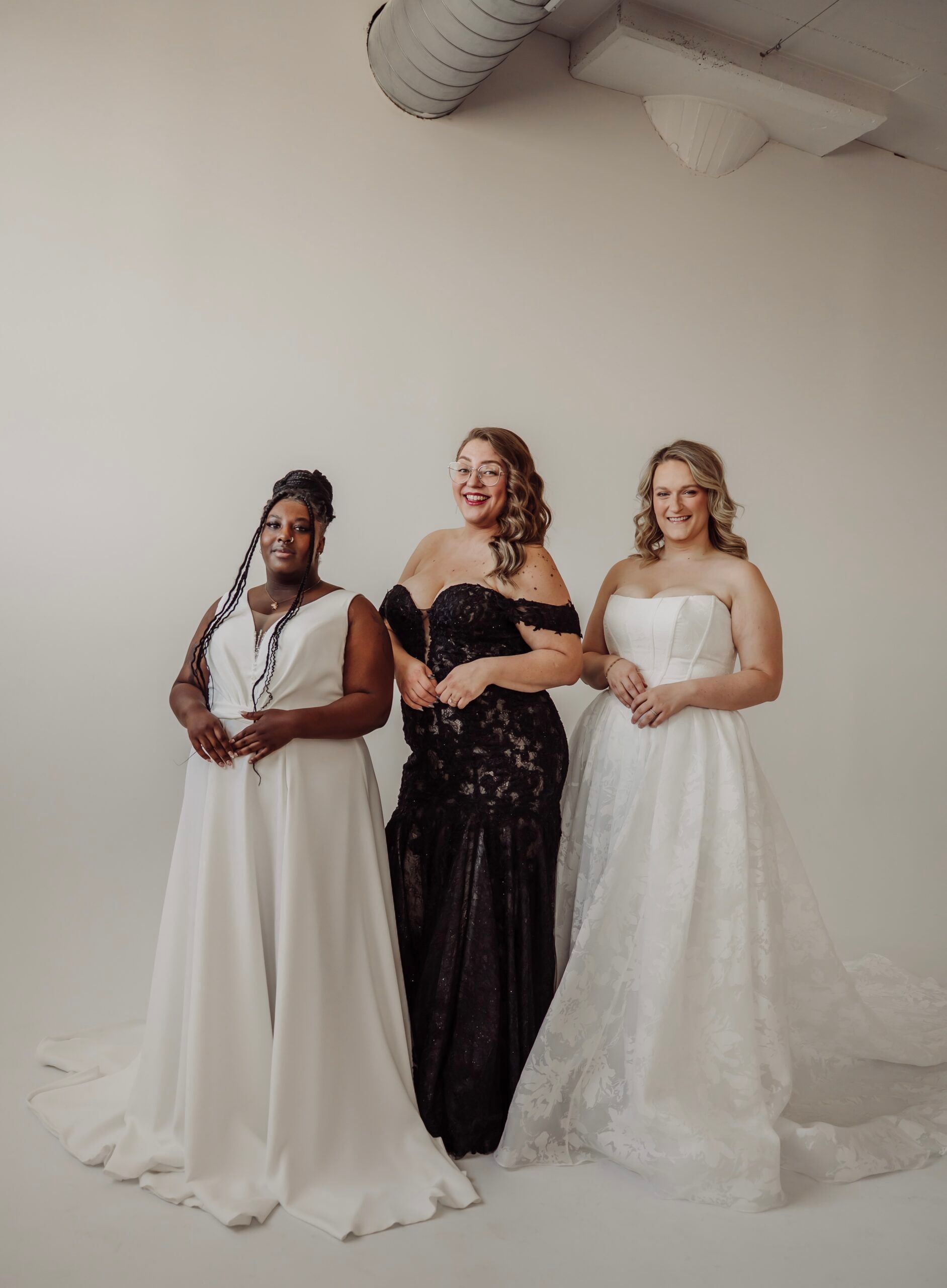 Three curvy women in plus size wedding dresses are standing next to each other in a room.