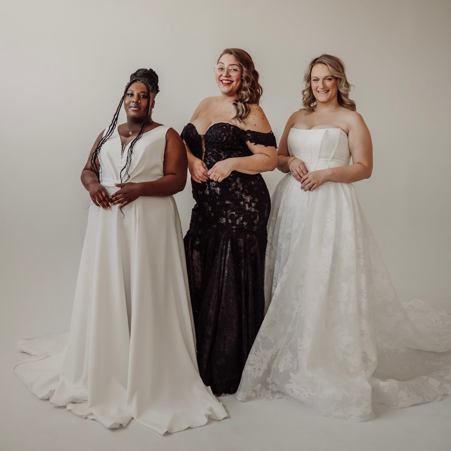 Three diverse women in wedding dresses are standing next to each other. One wedding dress is a black bridal gown.