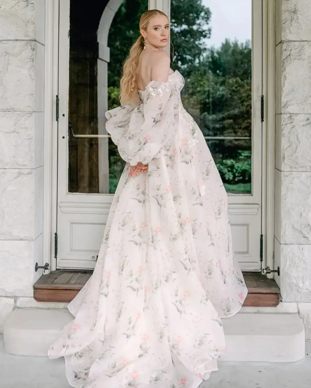 A woman in a floral dress is standing in front of a door.