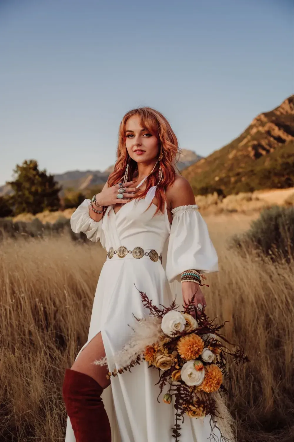 A woman in a white dress is standing in a field holding a bouquet of flowers.