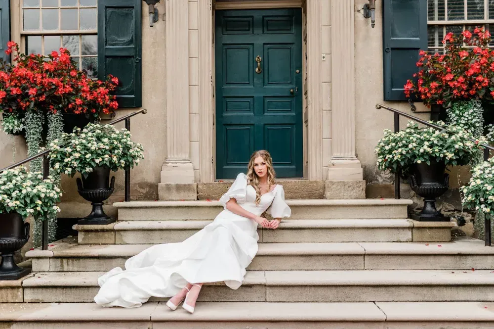 A woman in a wedding dress is sitting on the steps of a building.