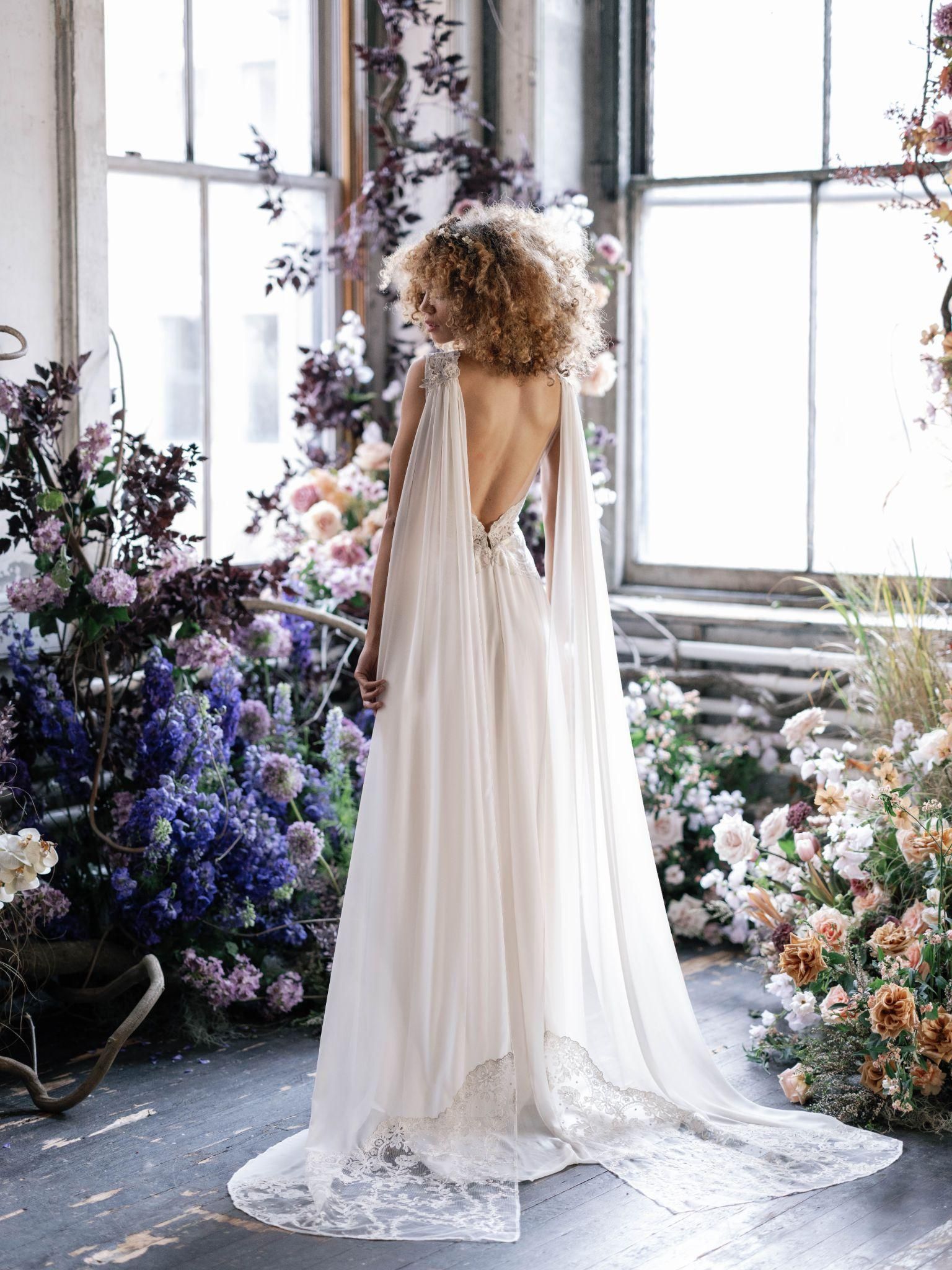 A woman in a wedding dress is standing in front of a window surrounded by flowers.