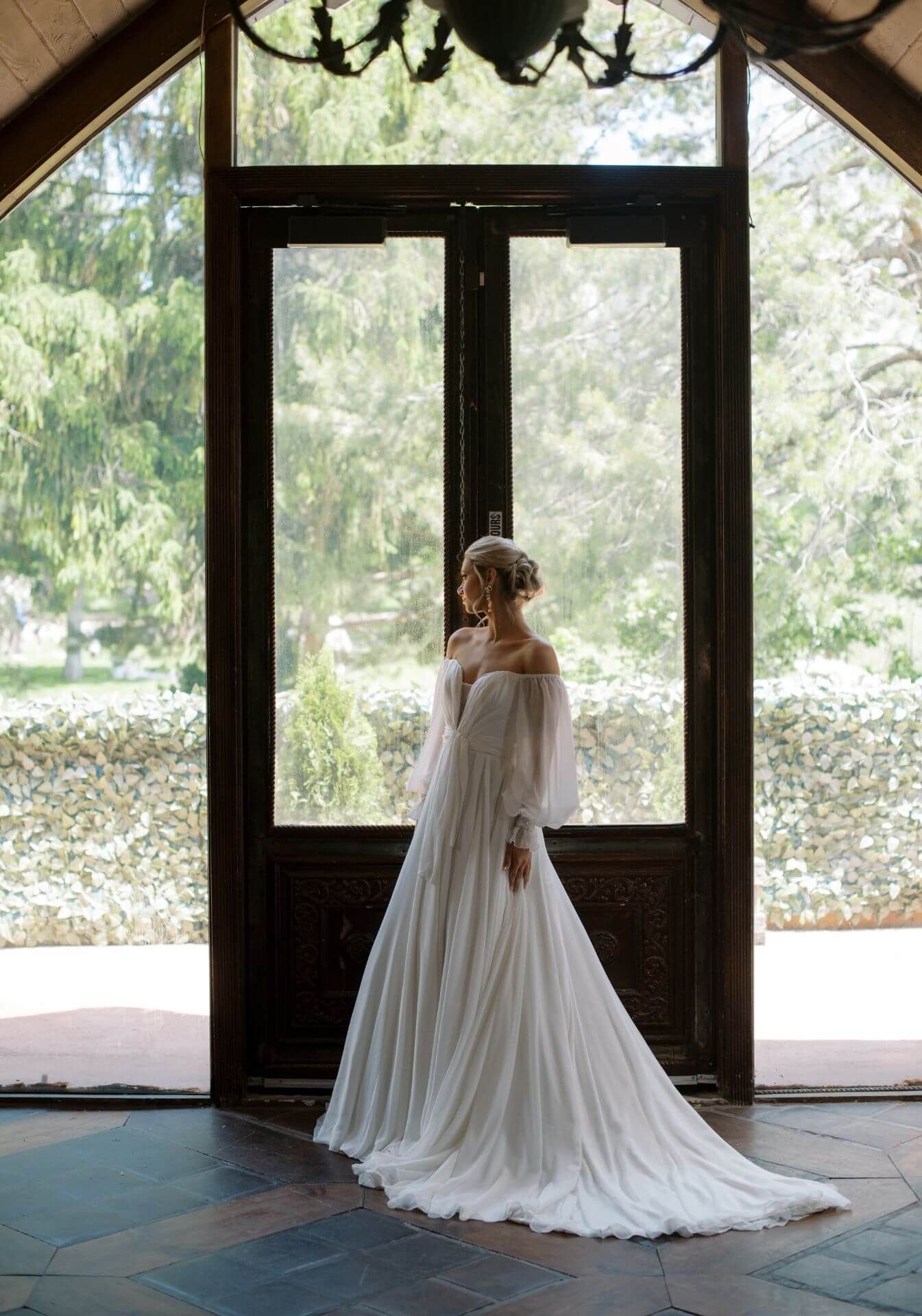 A woman in a wedding dress is standing in front of a window.