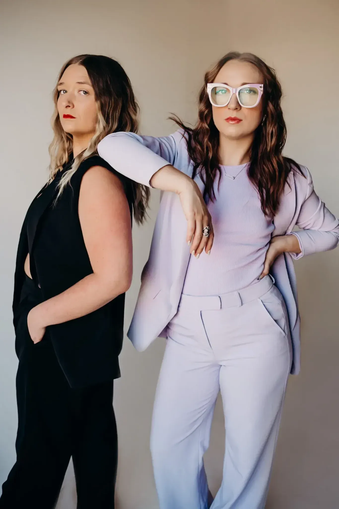 Two women are standing next to each other wearing suits and sunglasses.