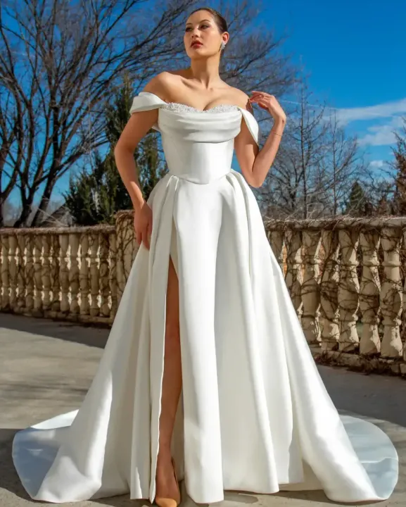 A woman is wearing a white Elizabeth Lee wedding dress with a high leg slit.