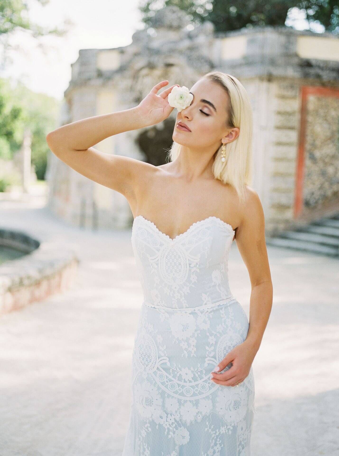A woman in a white dress is holding a white flower in her hand.