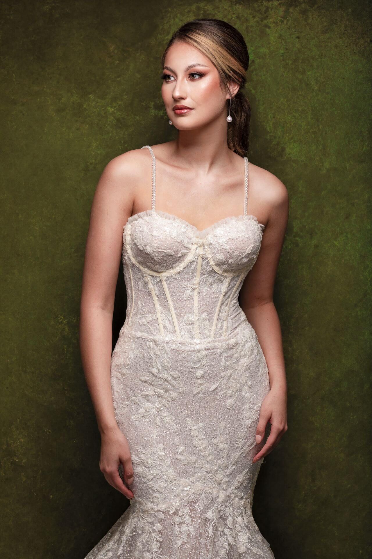 A woman in a wedding dress is standing in front of a green wall.