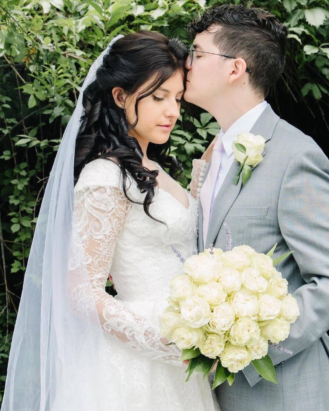 A bride and groom are kissing while the bride is holding a bouquet of white roses.