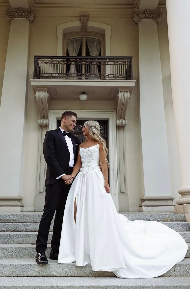 A bride and groom are standing on the steps of a building holding hands.