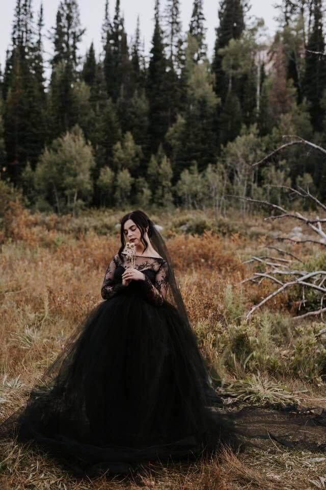 A woman in a black dress and veil is standing in a field.