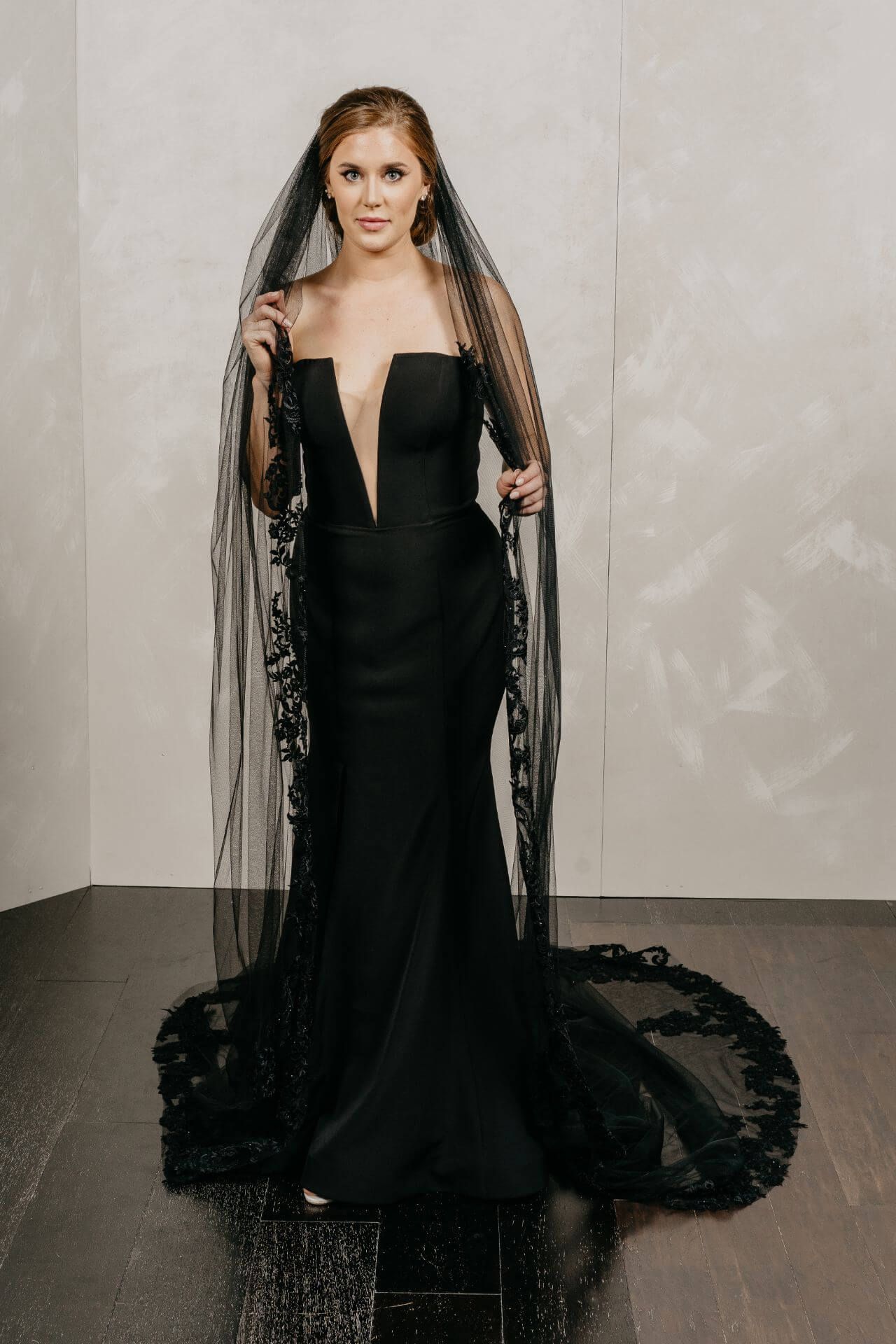 A woman in a gold wedding dress and gloves is standing next to a chair.