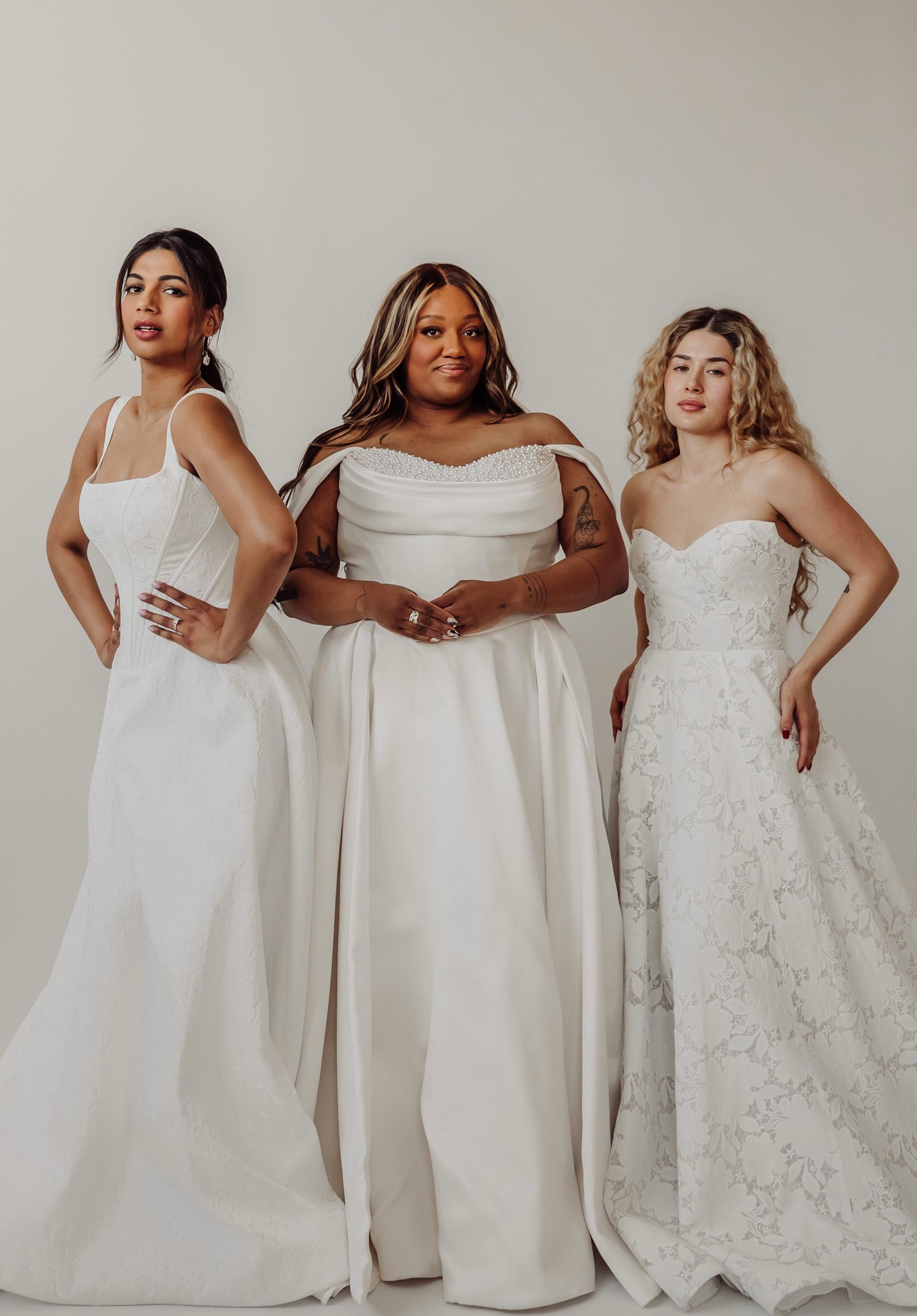 Three women in white wedding dresses, posing in front of a white background.
