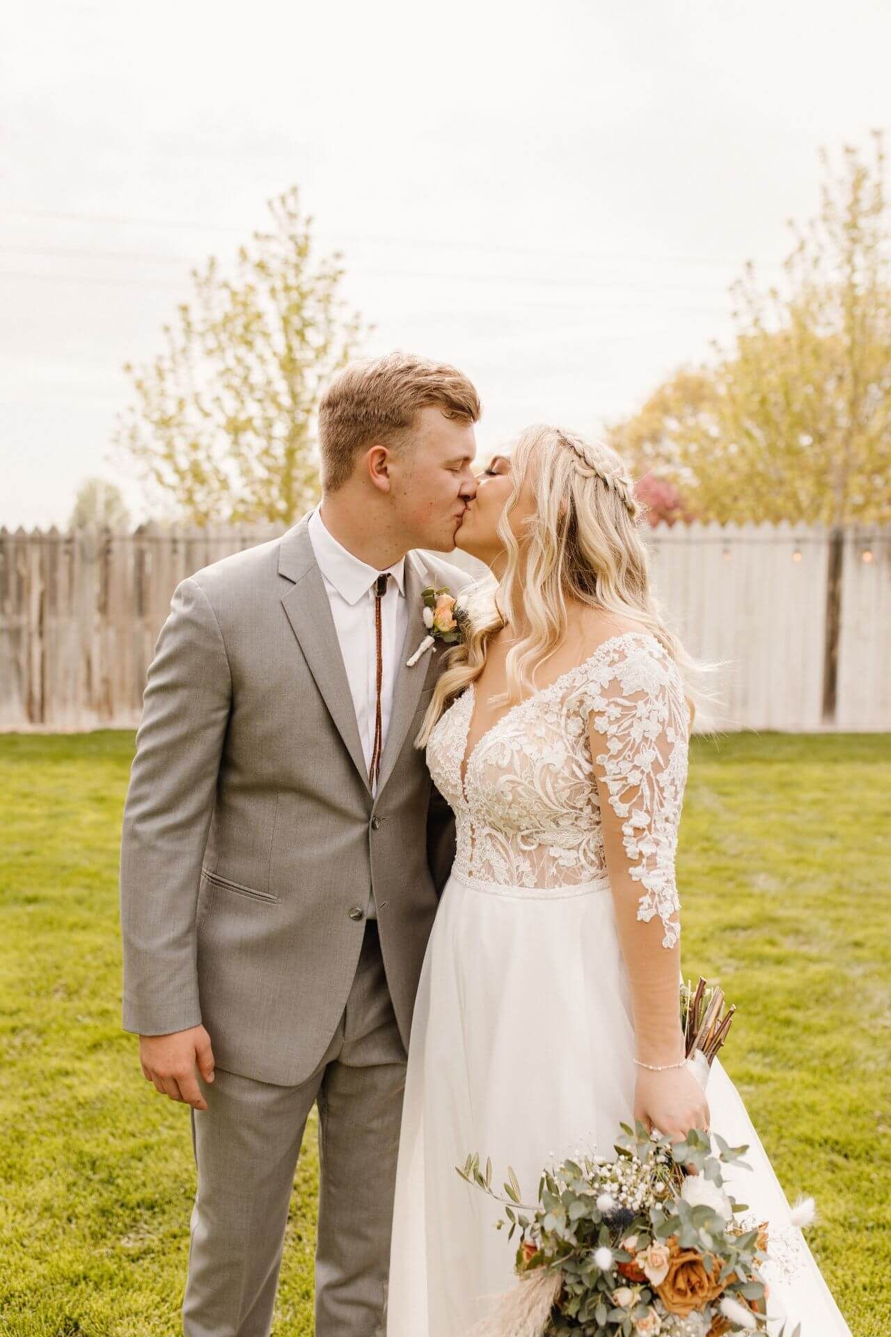 A bride and groom are kissing in a grassy field.